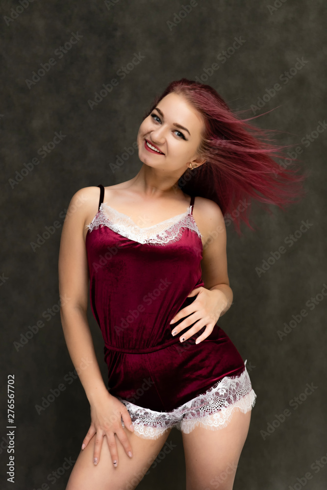 Concept portrait of a knee-high pretty sexy girl with purple hair in beautiful red lingerie on a gray background. She smiles, happy with life, happy. Hair flying, front view. Made in a studio. Concept portrait of a knee-high pretty sexy girl with purple hair in beautiful red lingerie on a gray background. She smiles, happy with life, happy. Hair flying, front view. Made in a studio.