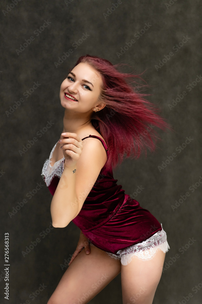 Concept portrait of a knee-high pretty sexy girl with purple hair in beautiful red lingerie on a gray background. She smiles, happy with life, happy. Hair flying, front view. Made in a studio. Concept portrait of a knee-high pretty sexy girl with purple hair in beautiful red lingerie on a gray background. She smiles, happy with life, happy. Hair flying, front view. Made in a studio.