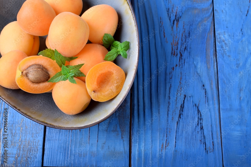 Ripe apricots in a ceramic bowl on the blue table Ripe apricots in a ceramic bowl on the blue table