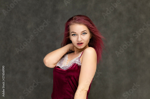 Concept portrait of a pretty sexy girl with purple hair in beautiful red lingerie on a gray background. She smiles, happy with life, happy. Hair flying, front view. Made in a studio.