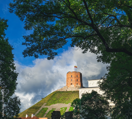 Gediminas tower with flag on hill in a beautiful summer day in Vilnius, Lithuania. Down side view of the tower among the tree branches photo