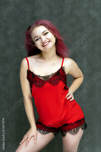 Concept portrait of a pretty sexy girl with purple hair in beautiful red lingerie on a white background. She smiles, happy with life, happy. Hair flying, front view. Made in a studio.