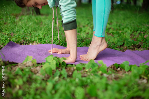 Thin brunette girl plays sports and performs yoga poses in a summer park. Green forest on the background. Woman doing exercises on the yoga mat, hands and feet close-up © Kate