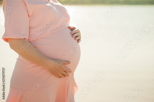 Male and female hands hold a pregnant belly closeup and copy space. Pregnant in a pink dress on a background of water