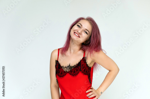 Concept portrait of a pretty sexy girl with purple hair in beautiful red lingerie on a white background. She smiles, happy with life, happy. Hair flying, front view. Made in a studio.