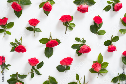 Floral pattern made of red roses flowers, green leaves, branches on white marble background. Flat lay, top view. Valentine's day background. Flowers pattern, floral composition.