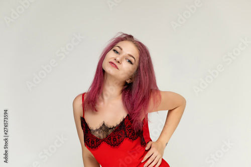 Concept portrait of a pretty sexy girl with purple hair in beautiful red lingerie on a white background. She smiles, happy with life, happy. Hair flying, front view. Made in a studio.
