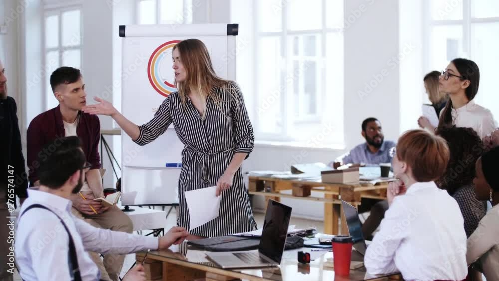 Happy young smiling blonde finance coach woman teaching multiethnic workers, leading team discussion at modern office. Happy young smiling blonde finance coach woman teaching multiethnic workers, leading team discussion at modern office.