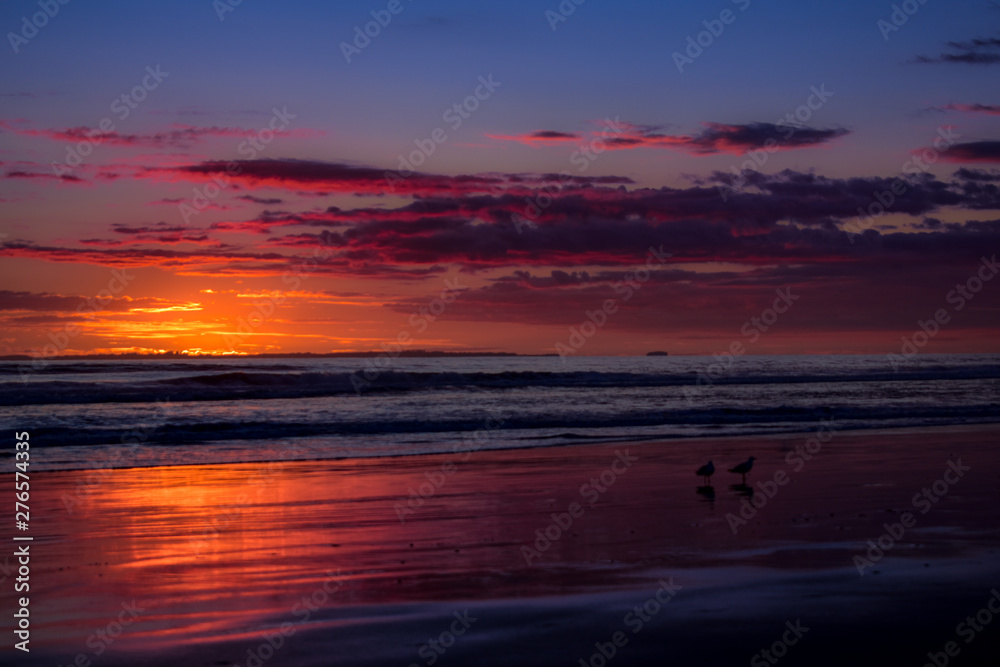 Sol saliendo en el horizonte, cielo naranja y playa vacia