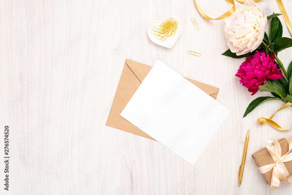 Flat lay home office desk. Female workspace with blank paper card, craft envelope, bouquet of peony flowers, golden accessories on wooden background. Top view feminine background. Fashion blog banner Flat lay home office desk. Female workspace with blank paper card, craft envelope, bouquet of peony flowers, golden accessories on wooden background. Top view feminine background. Fashion blog banner
