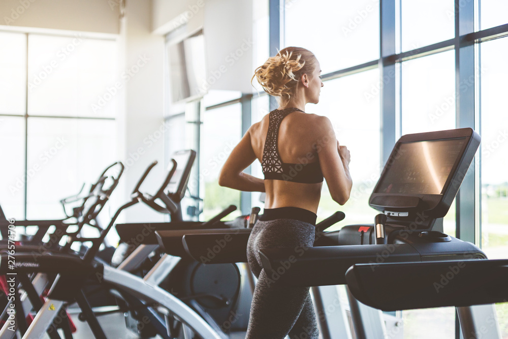 The athletic woman dressed in a black sportswear running on the treadmill in the modern gym
