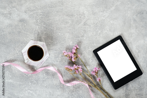 Flat lay elegant feminine accessories: coffee cup, pink ribbon, dry flowers and e book reader on concrete surface. Top view beauty blogger workspace, freelancer home office desk. Fashion blog hero. photo