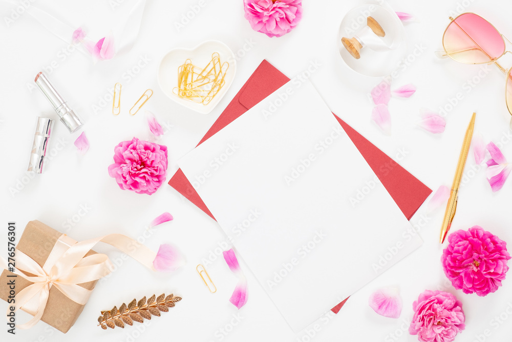 Flat lay home office desk. Top view blank paper card, pink rose flower buds, petals, female accessories, gift box on white background. Women desk, fashion blogger, beauty concept.