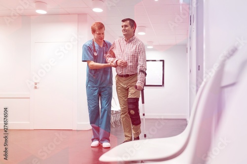 Nurse assisting patient with injured leg in walking at hospital corridor © moodboard
