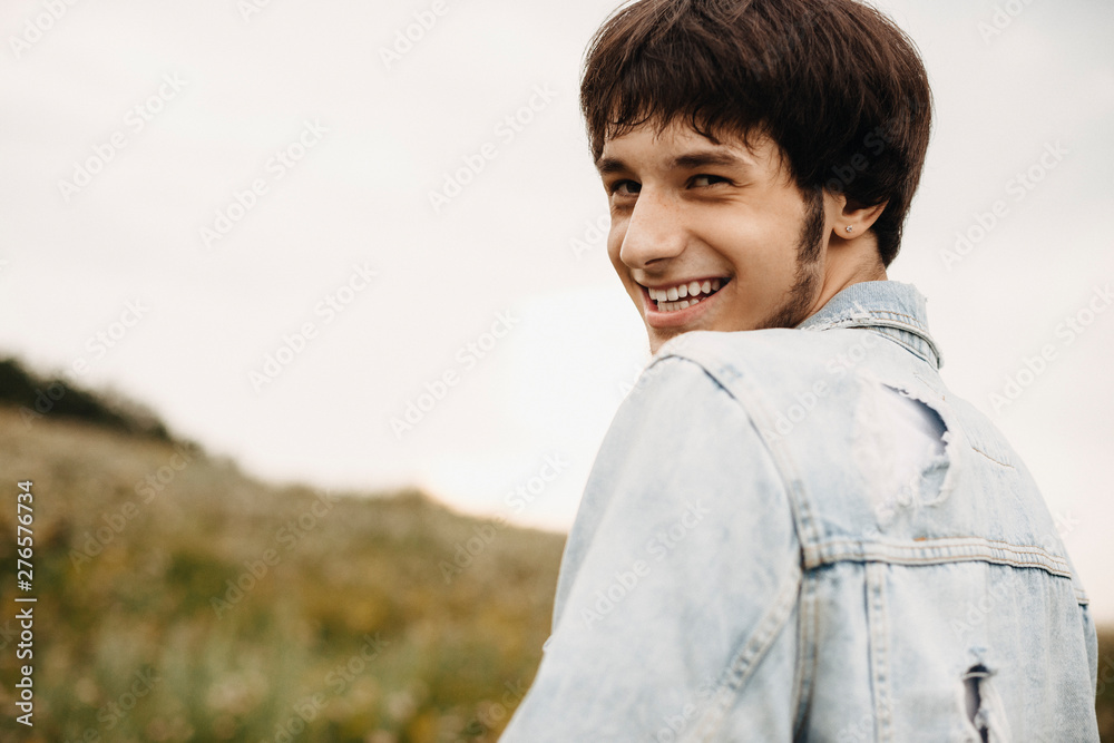 Portrait of a charming man dressed in jeans jacket looking over the shoulder laughing at camera outside. Portrait of a charming man dressed in jeans jacket looking over the shoulder laughing at camera outside.