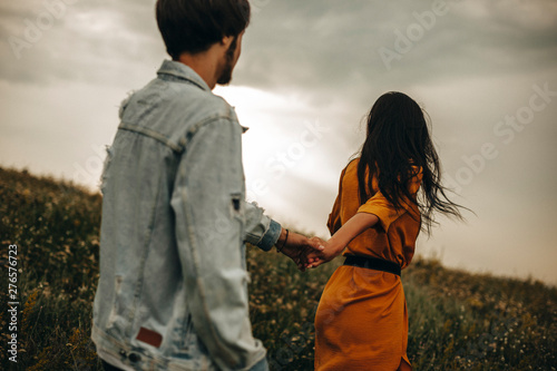 Back view of a amazing couple holding hands walking against a epic view on a field with flowers in their vacation time traveling. photo