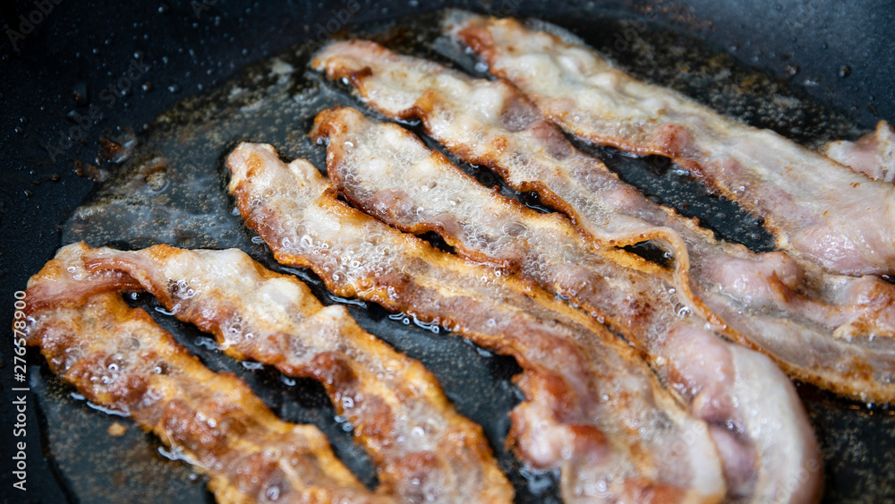 Slices of bacon baking on the pan, salt-cured pork Slices of bacon baking on the pan, salt-cured pork