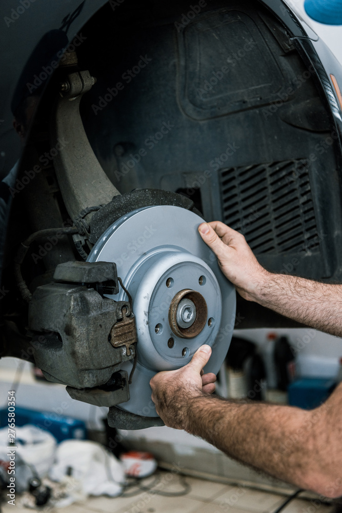 cropped view of auto mechanic holding metallic car brake near automobile cropped view of auto mechanic holding metallic car brake near automobile