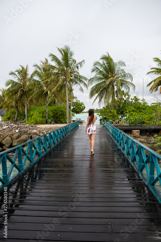 A young girl in a dress walking on a wooden bridge. The island is cloudy