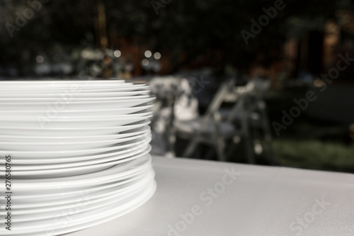 A stack of clean white plates stands on a table with a white tablecloth in the open air. Buffet at the party