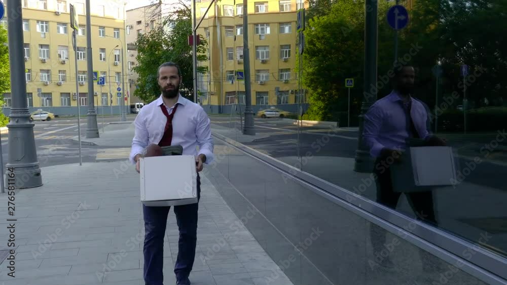 A dismissed handsome man with a beard, a manager in formal attire, upset after being fired, goes along with a box of personal belongings. Close-up, depression, bad mood, bad day.