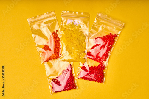 Embroidery items and tools. Colorful Japanese seed beads in bags on a yellow background