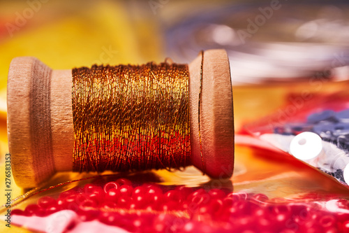 Embroidery products and tools. The spool of metallic thread, Japanese seed beads and sequins on a yellow background