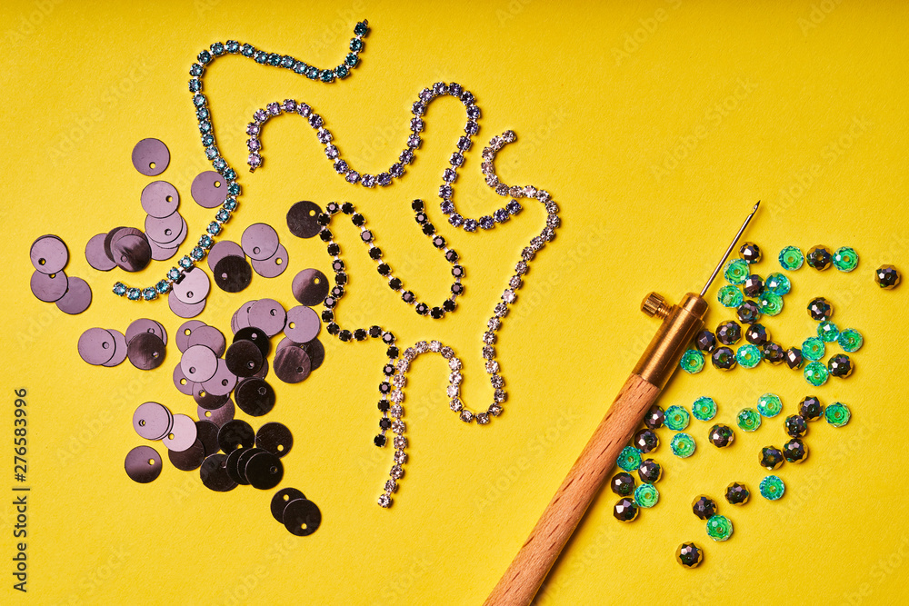 Fototapeta premium Embroidery products and tools. Black sequins, rhinestones and Luneville hook on a yellow background