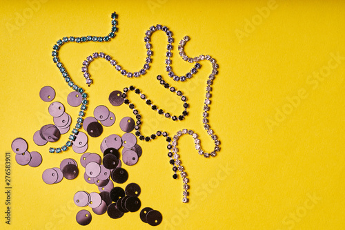 Embroidery products and tools. Black sequins and rhinestones on yellow background photo