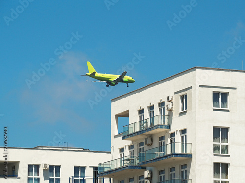 Passenger airplane flying over residential houses. Air transport takeoff or landing at blue sky background