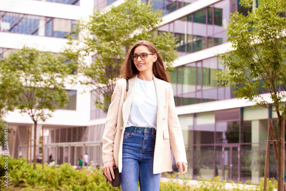Smiling young businesswoman walking on the street near office buildings