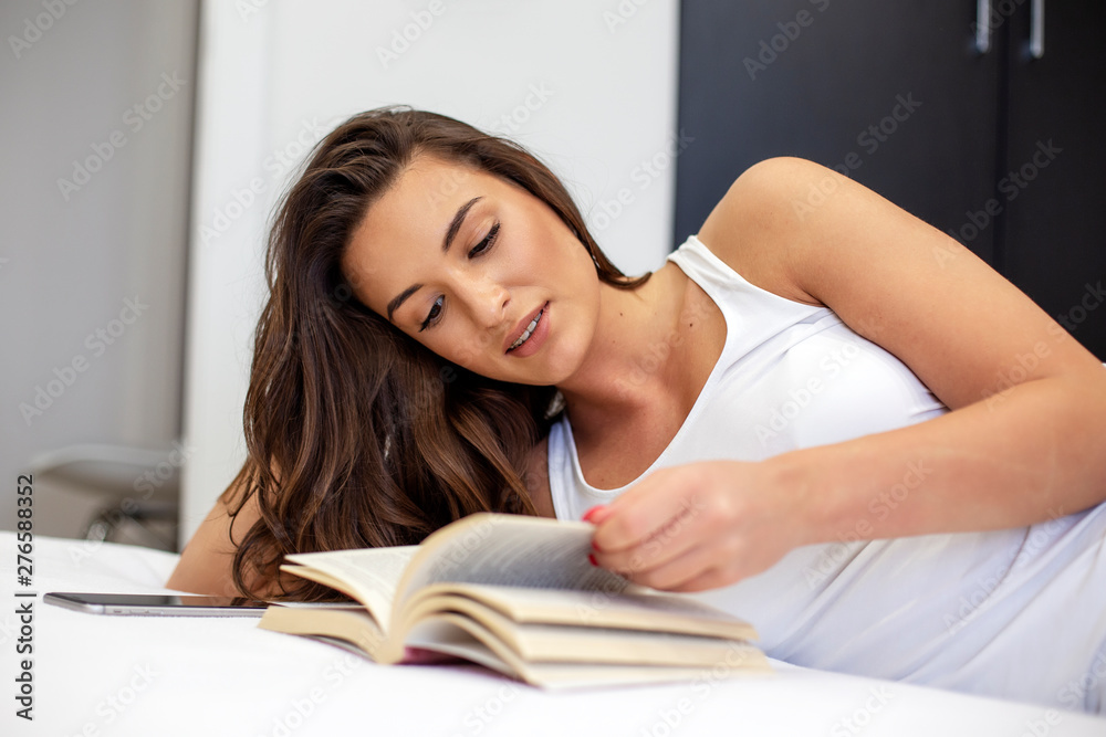 Young beautiful girl lying in bed and read book at morning Young beautiful girl lying in bed and read book at morning