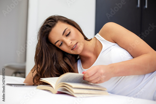 Young beautiful girl lying in bed and read book at morning