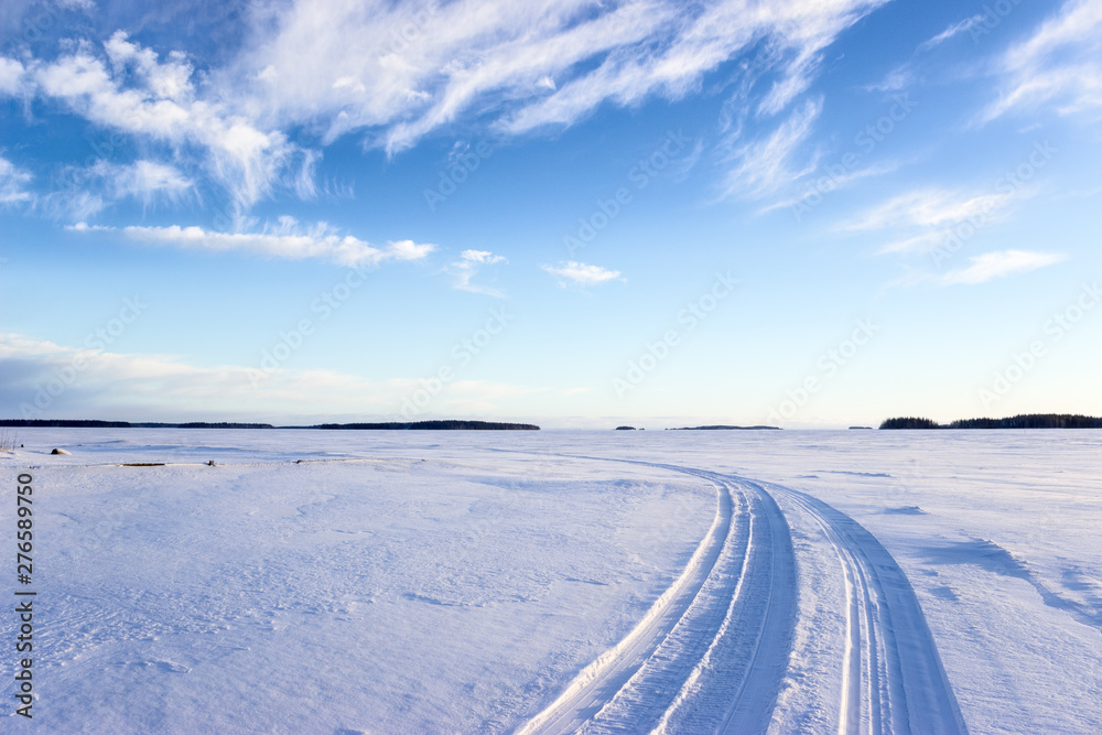 Road on snow and ice of frozen lake, tracks going to distance, sunny cold weather