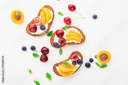 Summer toast snack bread, apricots, blueberries, cherries, basil leaves, curd cheese, sour cream, honey. Toasts sandwiches canapes healthy balanced meals Top view.