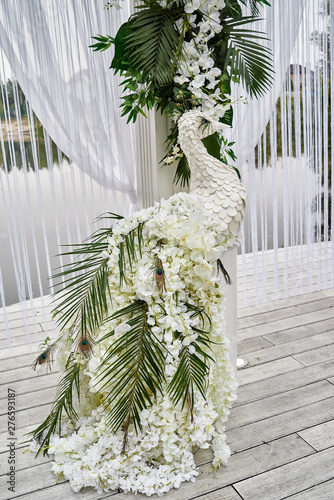 Luxury floral decor for wedding ceremony with palm leaves, orchid flowers and peacocks near water outdoors, copy space. Wedding arch decorations photo