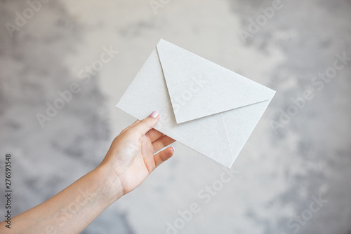 Female hand gives white envelope a wedding invitation on a gray background.