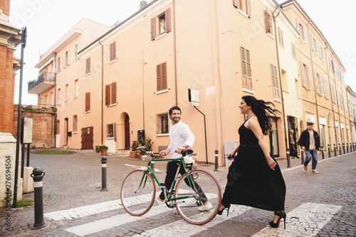 Beautifully dressed man and woman are walking in the old city with a bicycle. Love story in Rimini, Italy