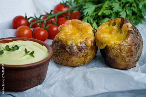Baked new potatoes wrapped in bacon, on top cheese, microgreen, sauce and fresh vegetables. Dark background.
