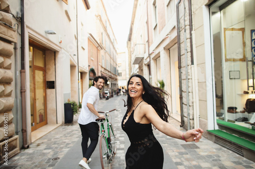Beautifully dressed man and woman are walking in the old city with a bicycle. Love story in Rimini, Italy