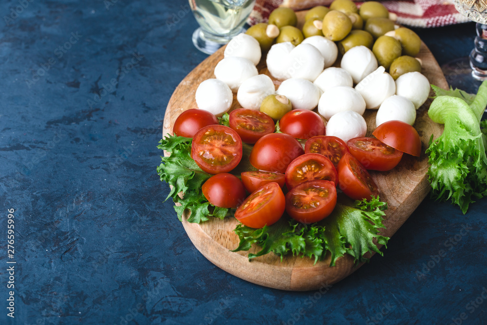 summer snack of mozzarella, tomatoes, olives and greens on wooden board. Dark blue background. Horizontal, place for text summer snack of mozzarella, tomatoes, olives and greens on wooden board. Dark blue background. Horizontal, place for text
