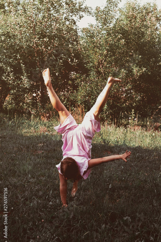 Young girl in pink clothes is standing upside down on one hand. Future gymnast and happy childhood concept. Summer sports fun. Authentic atmosphere