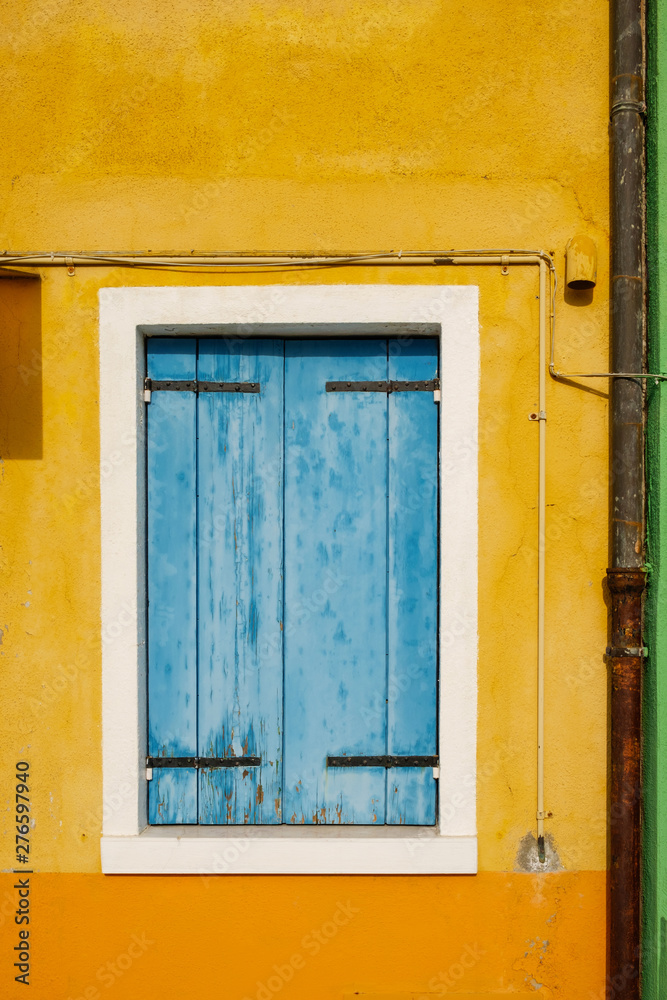 Old window with blue wooden closed blinds on the shabby yellow wall
