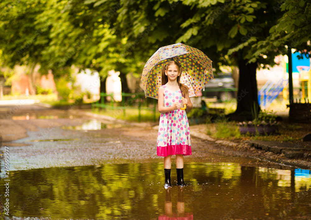 happy child girl in dress with an umbrella and rubber boots in puddle on summer walk