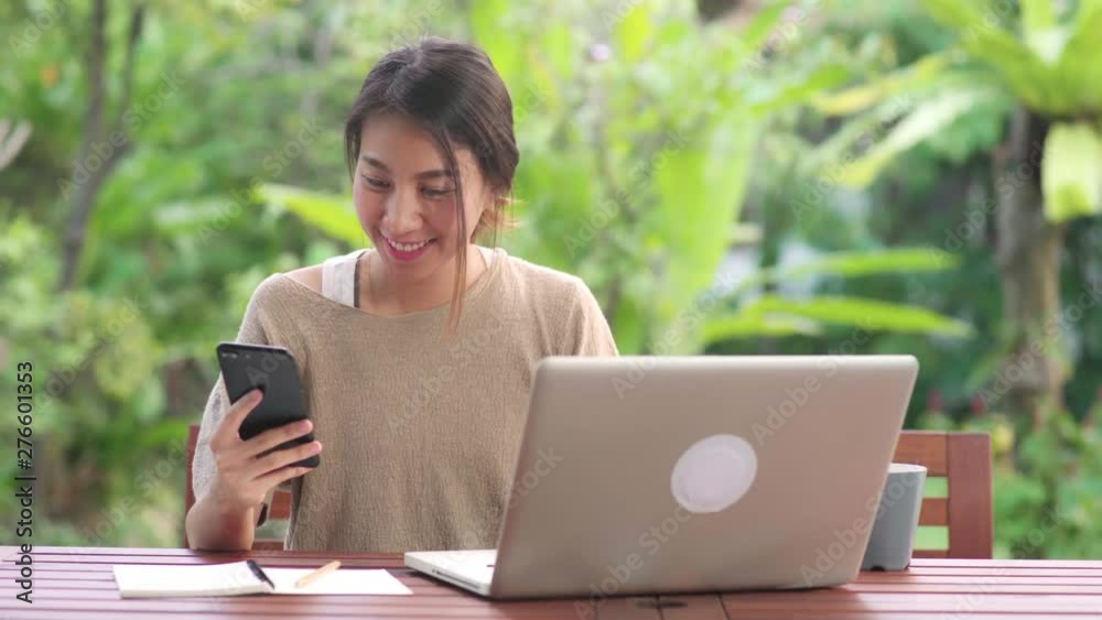 Freelance Asian woman working at home, business female working on laptop and using mobile phone drinking coffee sitting on table in the garden in morning. Lifestyle women working at home concept. Freelance Asian woman working at home, business female working on laptop and using mobile phone drinking coffee sitting on table in the garden in morning. Lifestyle women working at home concept.