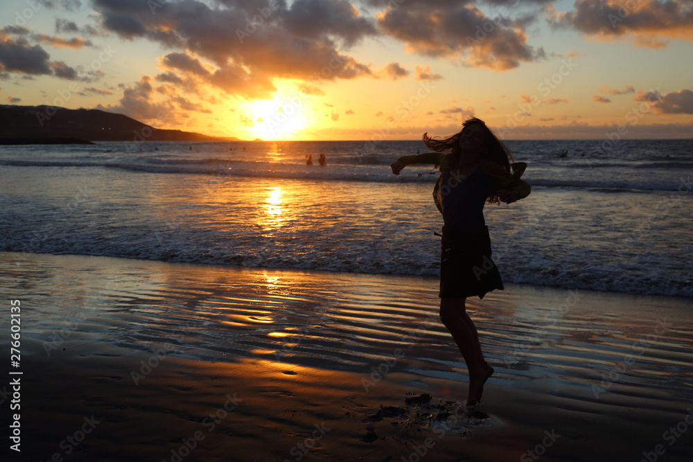Mujer caucásica en contra luz en la playa con atardecer de naranja intenso. Las palmas de gran canaria. España. Siluetas. Felicidad.