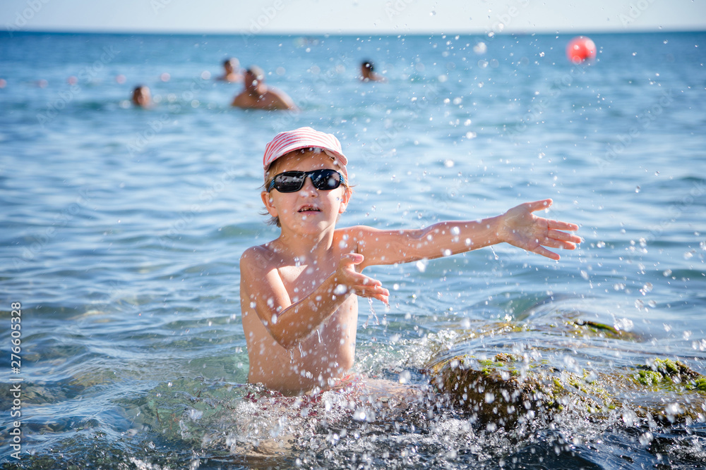 Boy splashing water during summer holidays. Attractive child having fun on a tropical beach, playing with stones and water.