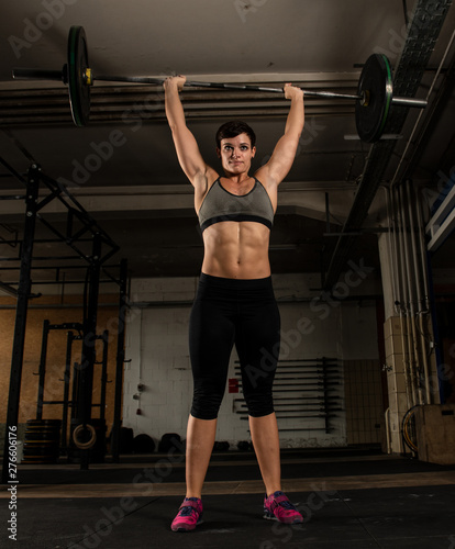 Junge hübsche Frau im Workout. Die athletische Sportlerin macht Krafttraining und strengt sich beim Training an. Über Kopf Gewichtheben mit der Langhantel.  © Julia43