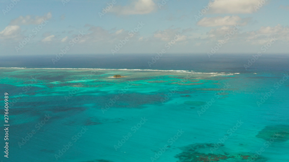 Top view of turquoise water of the atoll against the backdrop of the tropical island and sky with clouds. Travel concept.