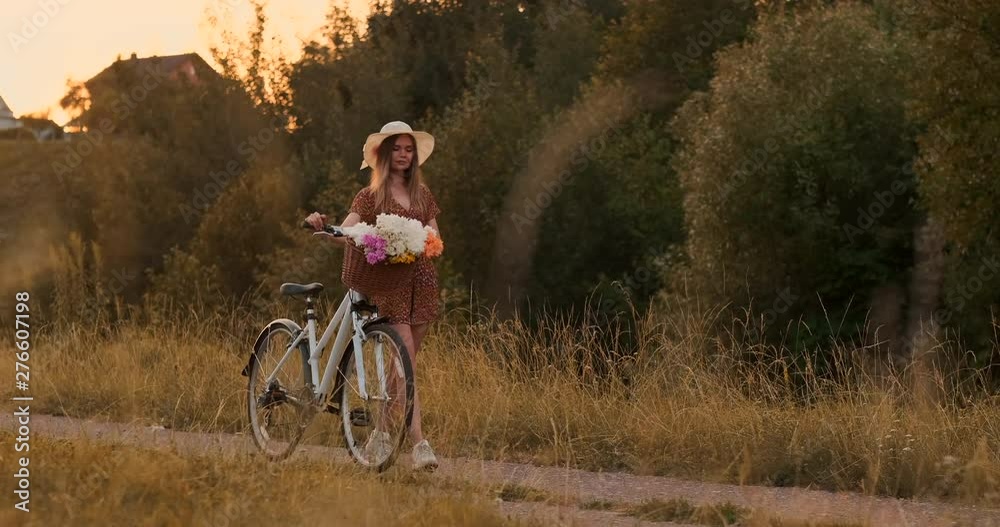 Summer in the field girl with flowers and a hat goes with a bike on the road Summer in the field girl with flowers and a hat goes with a bike on the road